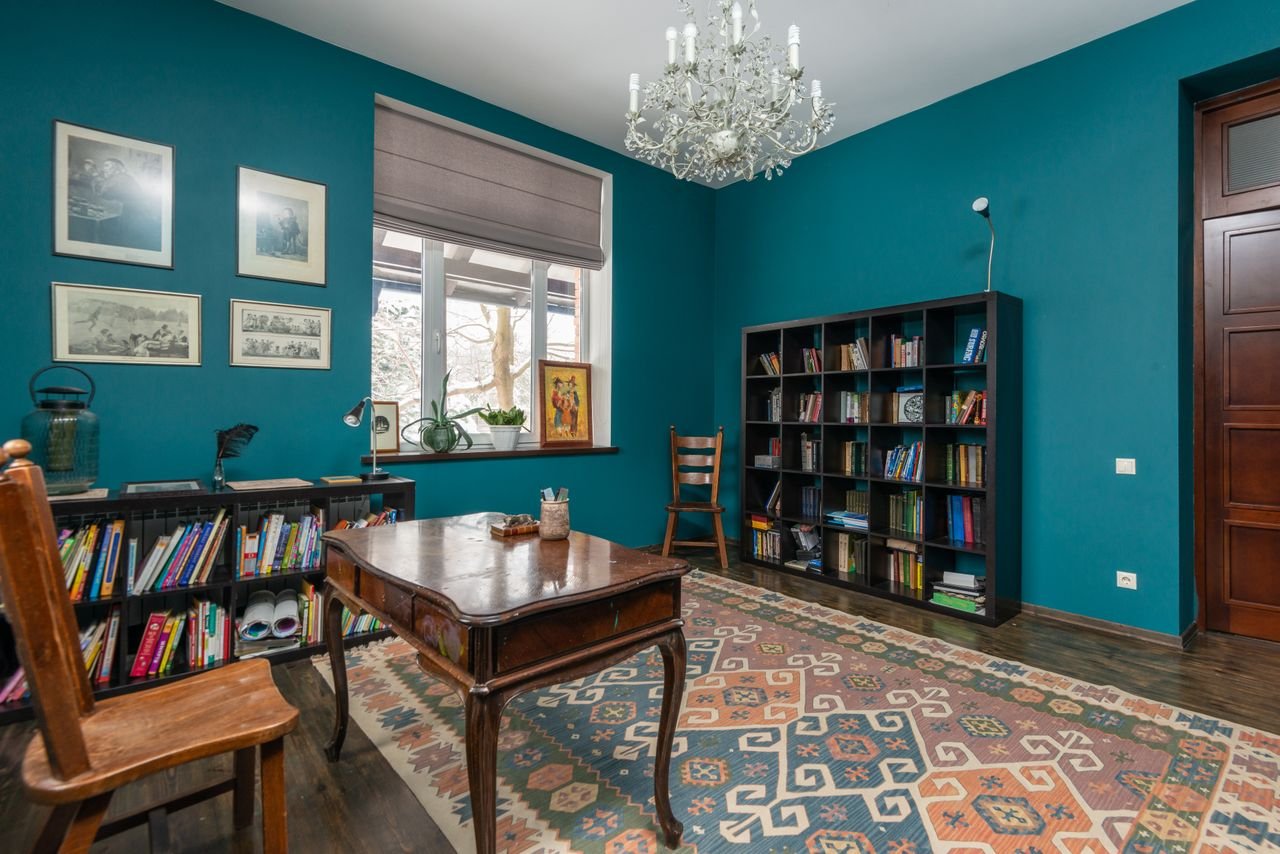 Vintage styled room with wooden chair at table placed on carpet near books on shelves at blue walls and window
